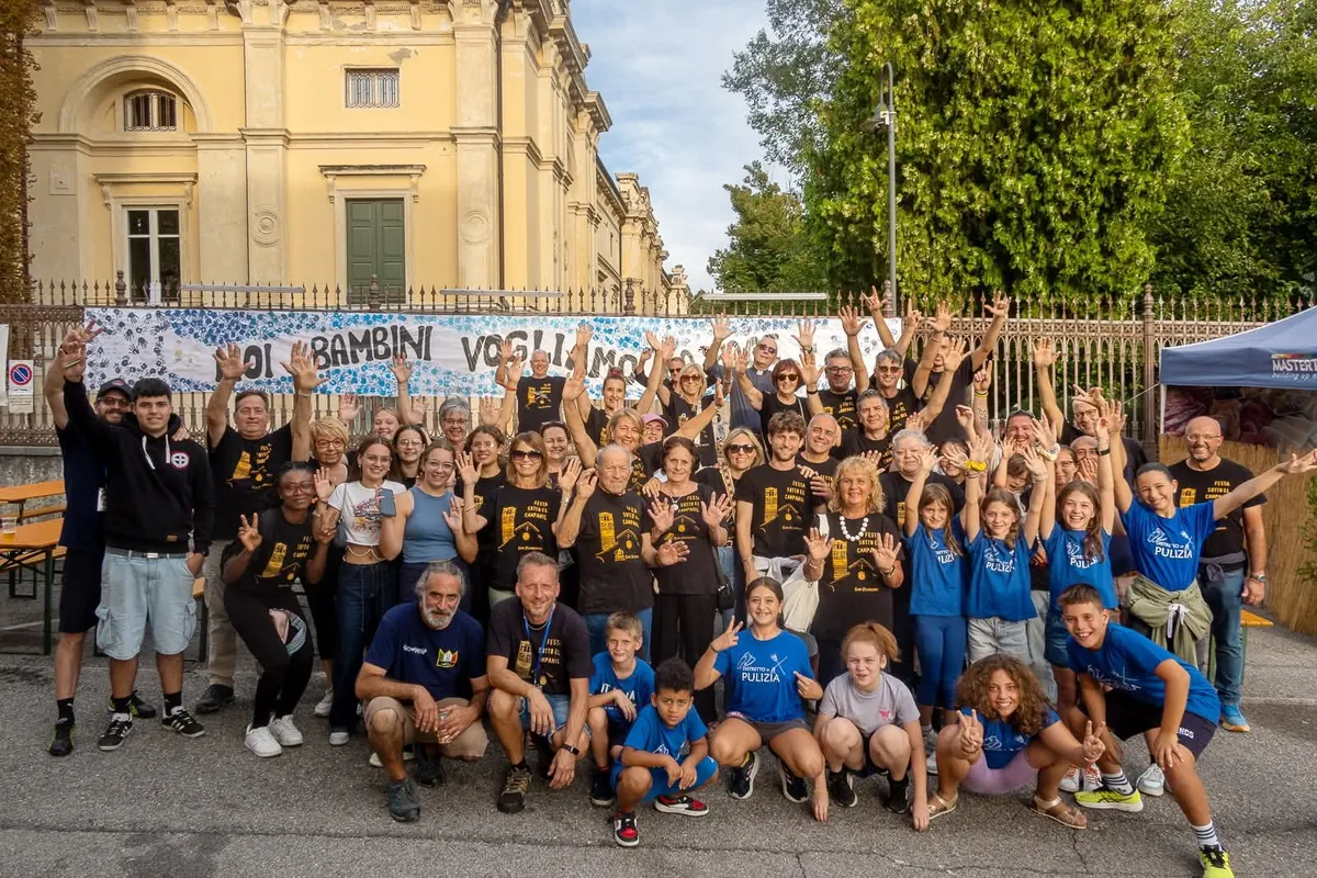 Volontari e bambini a braccia alzate davanti a Villa Lebrecht, con lo striscione dipinto dai bambini